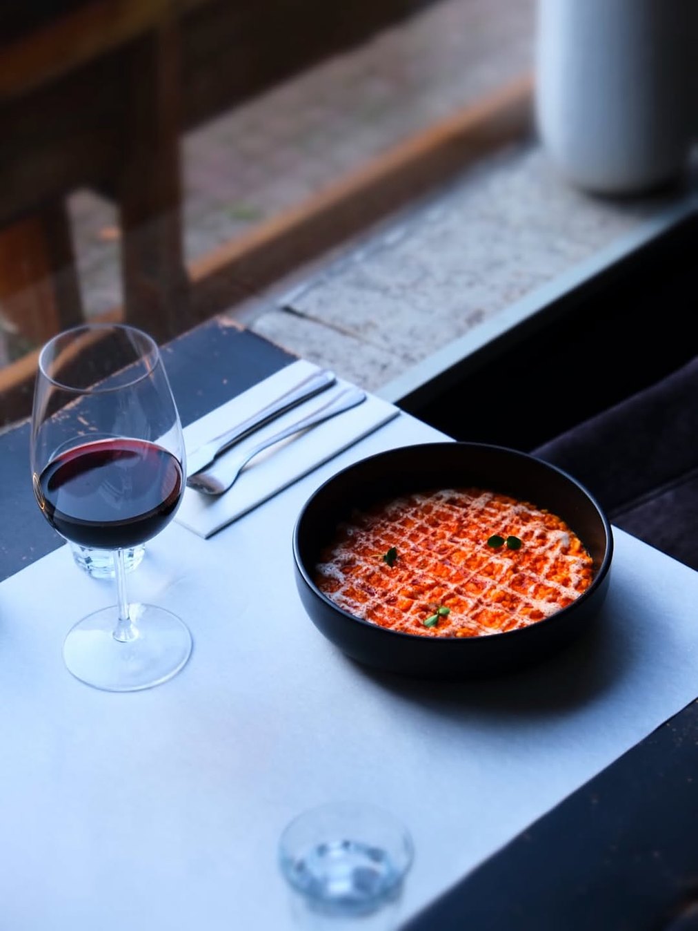 Gerecht in een zwarte kom met een glas rode wijn bij het raam