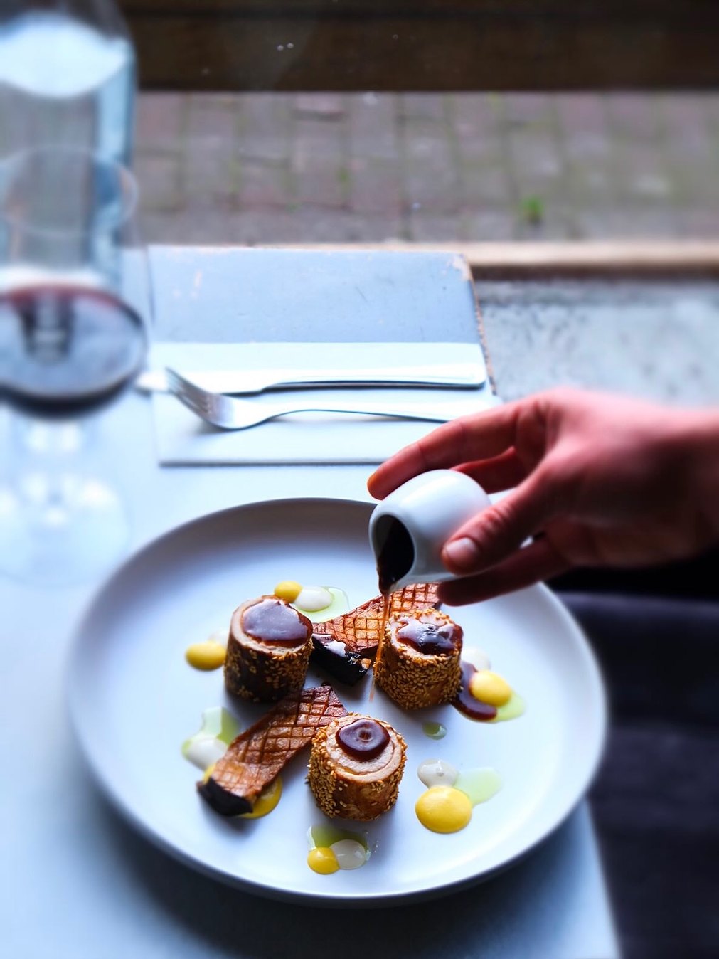 Saus wordt over het gerecht met sesamrolletjes geschonken
